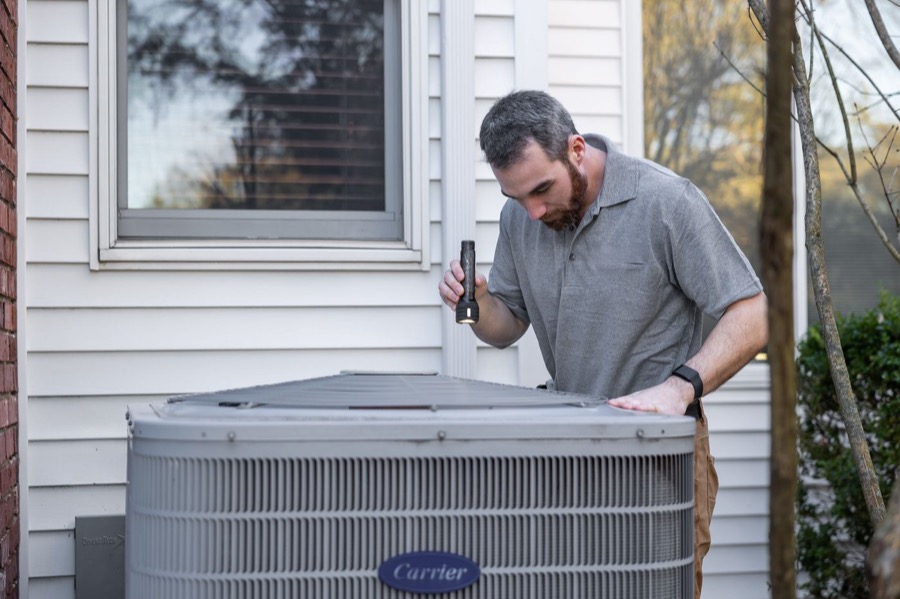 Kenyon & Sons technician inspecting an outdoor air-conditioning condenser unit